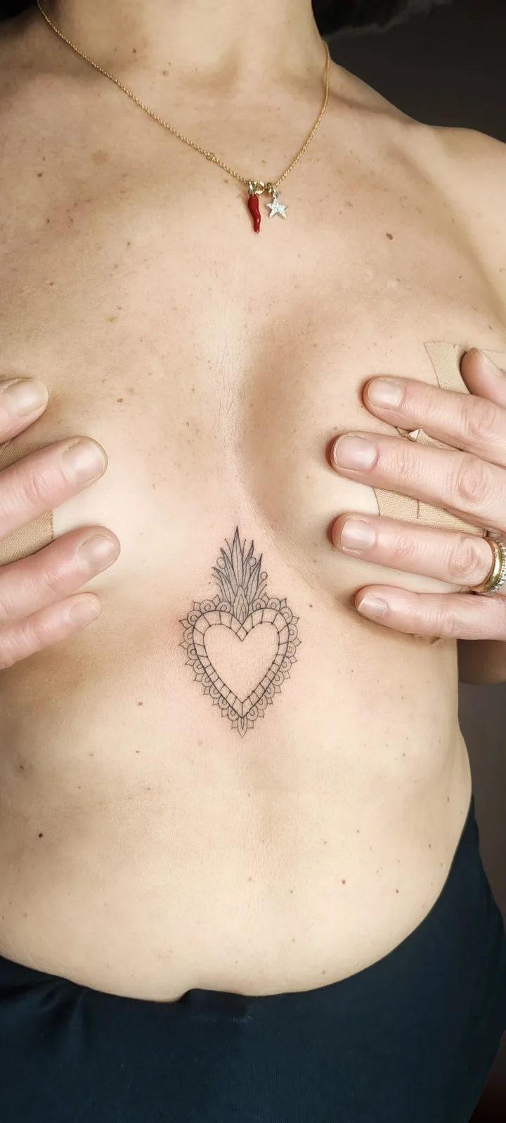Tatuaggio sullo sterno: un sacro cuore con la cornice decorata a motivi geometrici e la fiamma sopra, a linea sottile.
