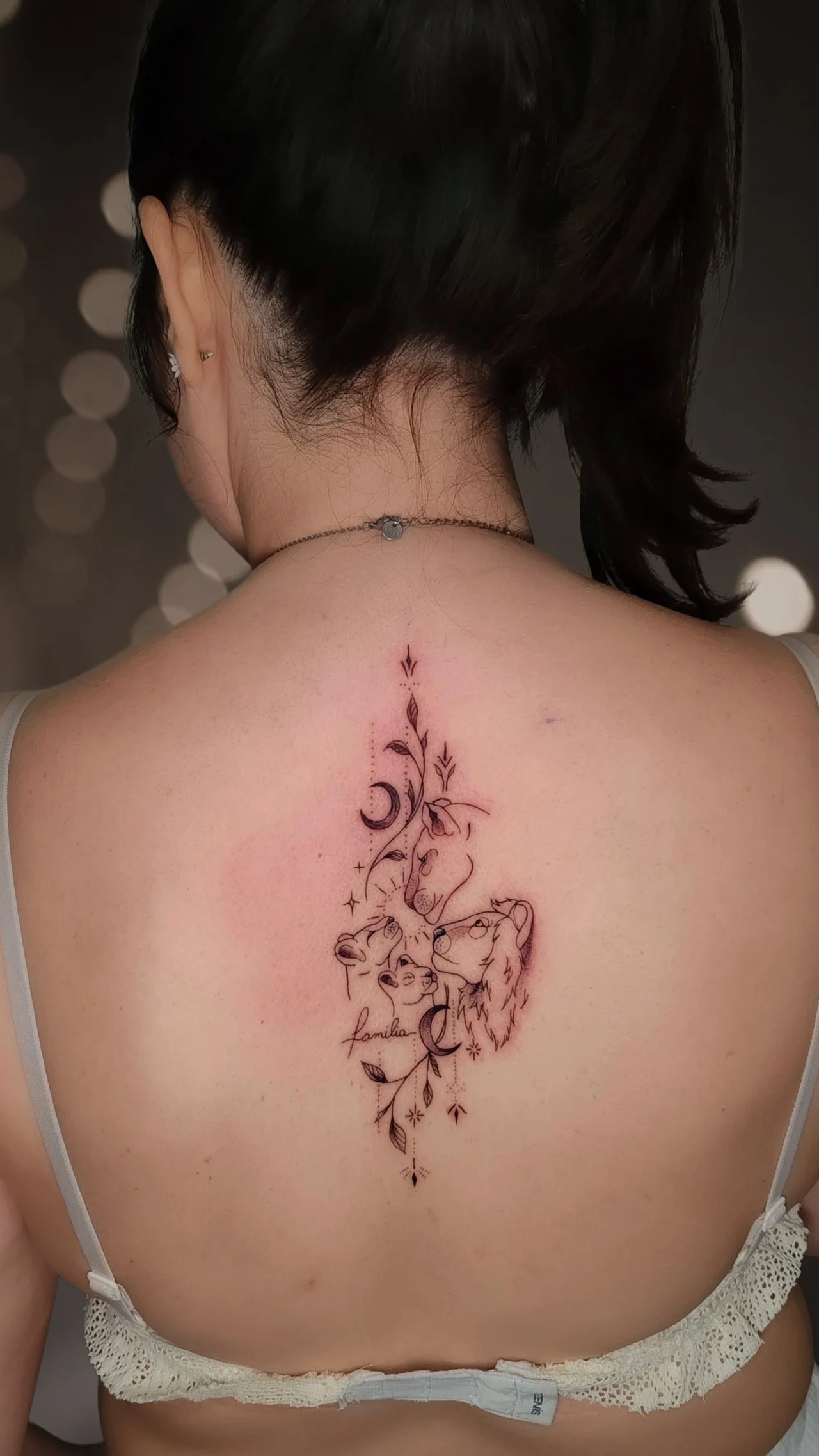 Tatuaggio sulla schiena: una leonessa con due cuccioli tra rami, lune e stelline, con la scritta «família» in corsivo.